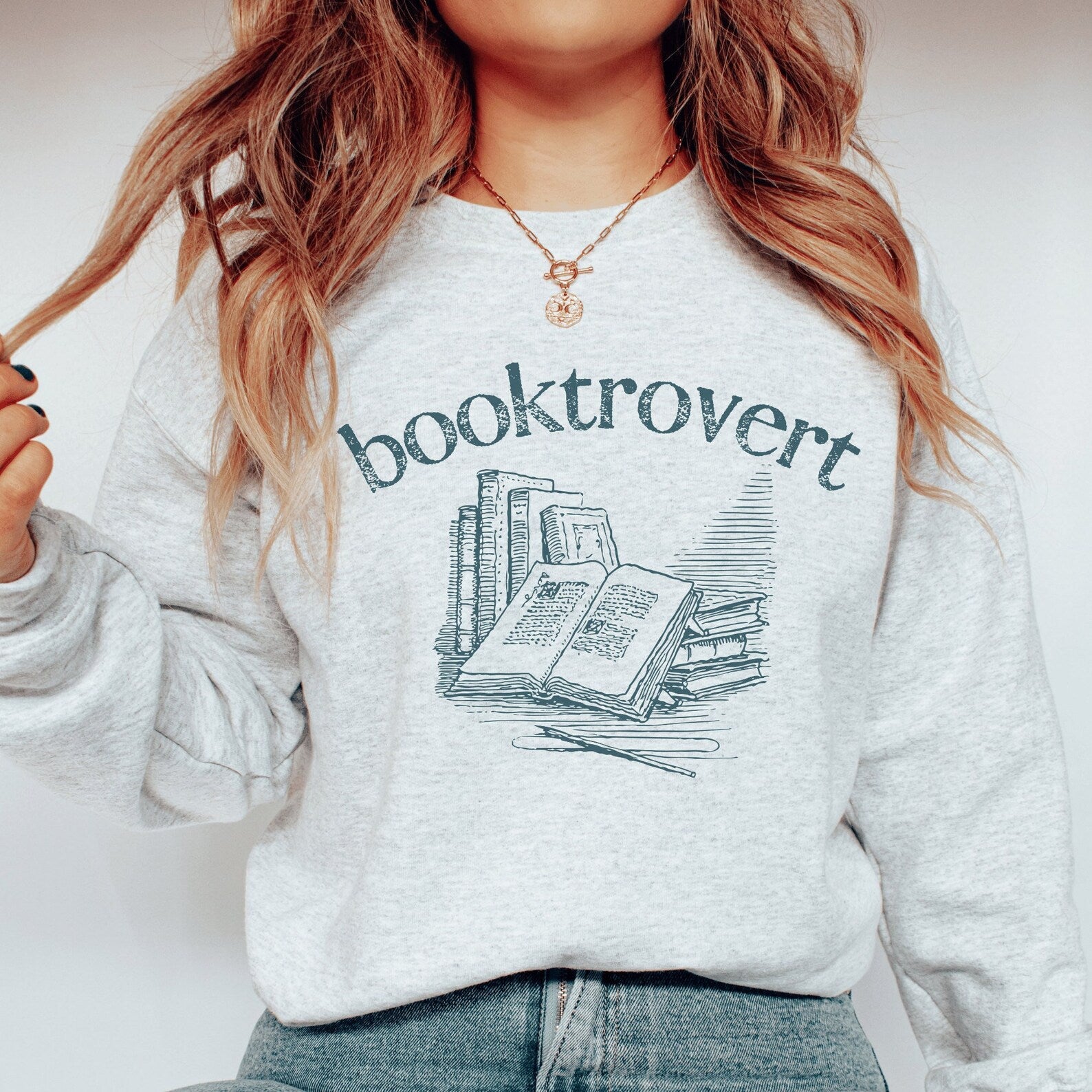 light gray ash unisex booktrovert shirt that says booktrovert in navy blue writing along with a graphic of books, perfect bookish merch for book lovers