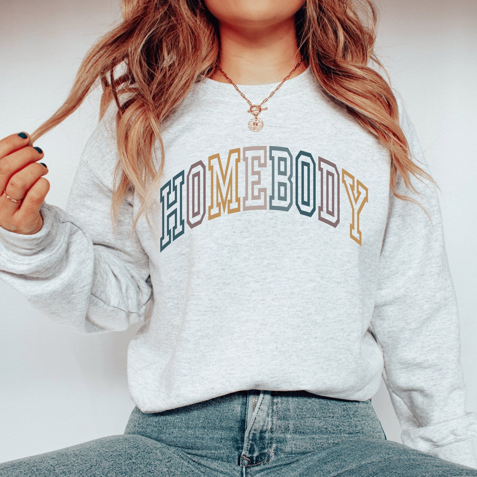 Ash gray unisex homebody sweatshirt, with the word homebody in multicolor lettering and college style font