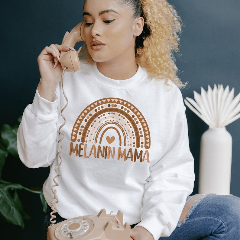 white  unisex melanin mom sweatshirt with a graphic of a rainbow in shades of brown with the words melanin mama underneath the rainbow