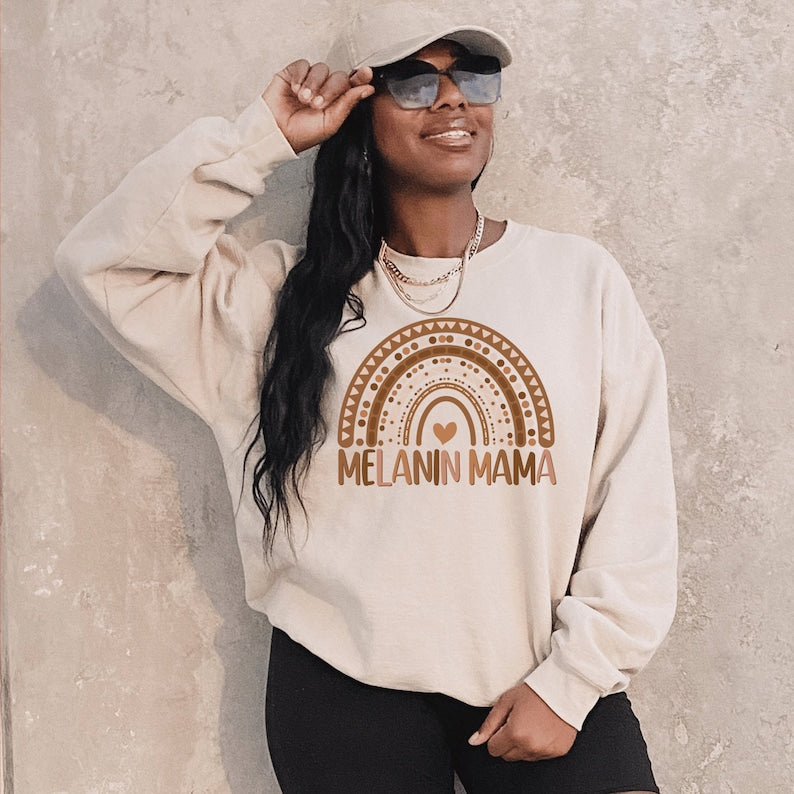 beige unisex melanin mom sweatshirt with a graphic of a rainbow in shades of brown with the words melanin mama underneath the rainbow