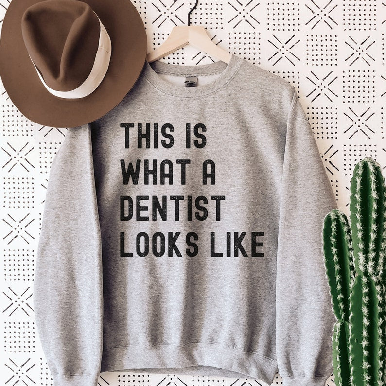 gray unisex dentist sweatshirt that says this is what a dentist looks like in all black, capital letters