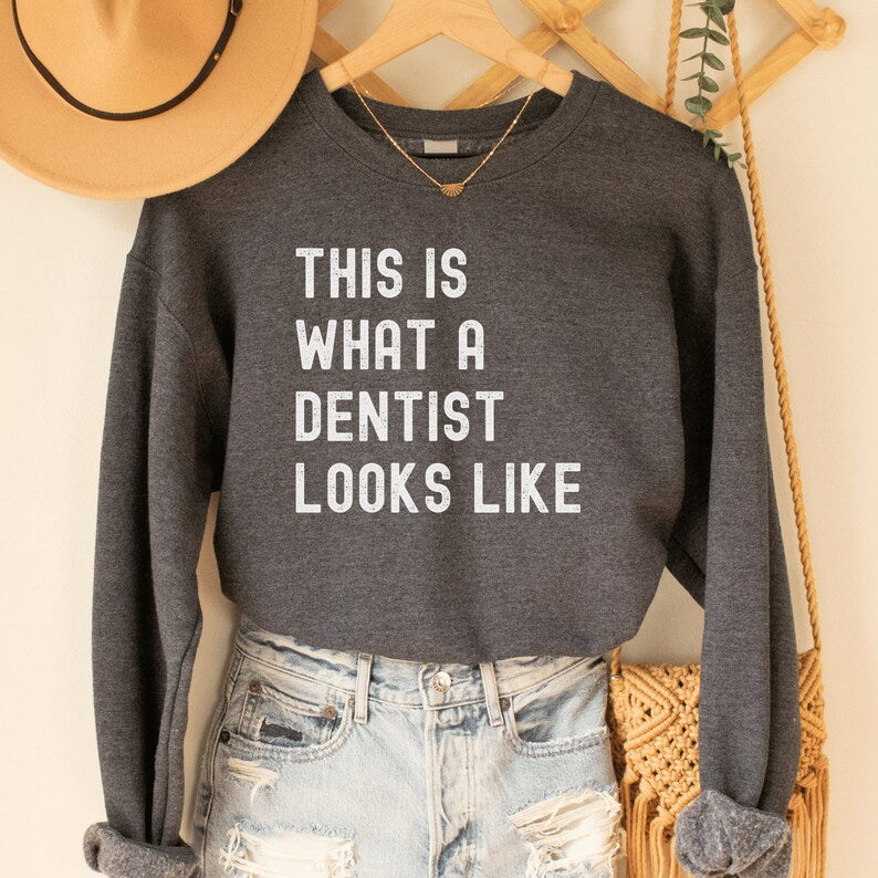 dark heather gray unisex dentist sweatshirt that says this is what a dentist looks like in all white, capital letters