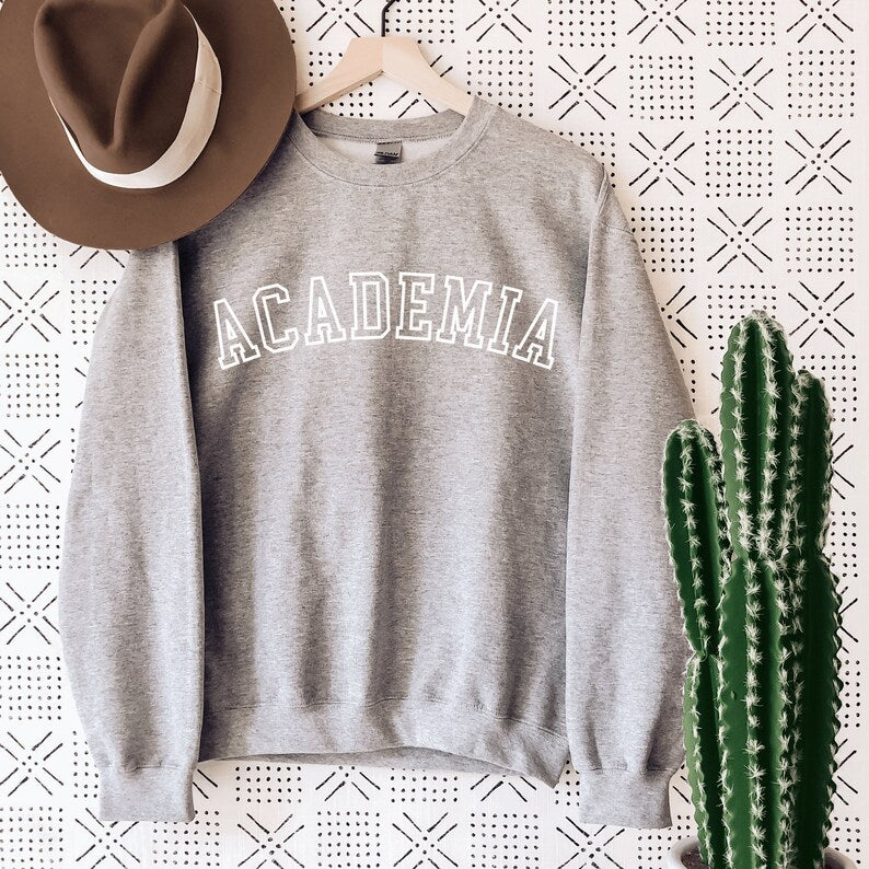 professor gifts, gray unisex sweatshirt on a female model that says Academia across the front in college style white letters