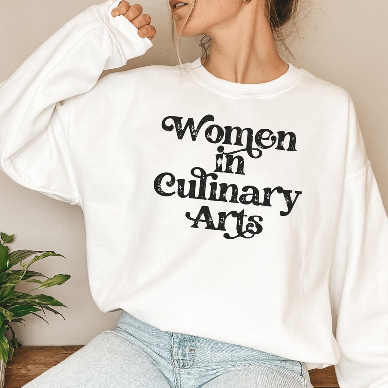 white unisex sweatshirt that says women in culinary arts in black letters with a whimsical font; perfect gift for culinary students