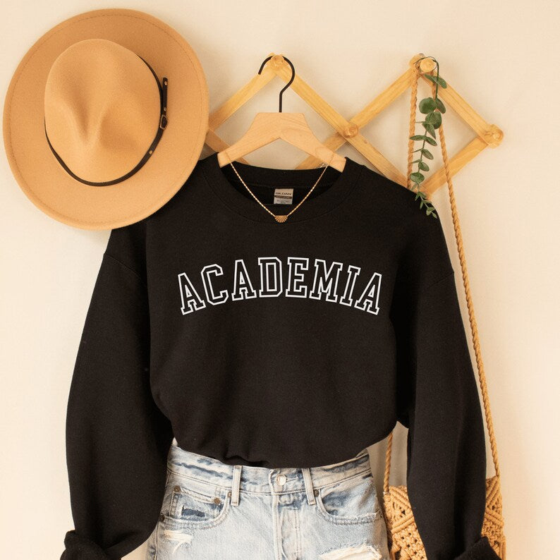 professor gifts, black unisex sweatshirt on a female model that says Academia across the front in college style white letters