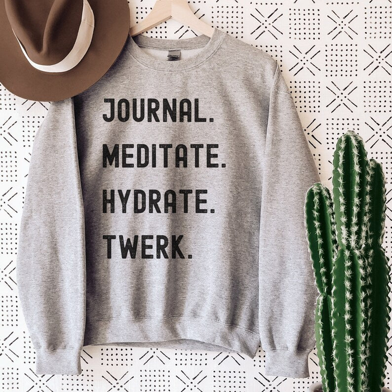 gray unisex sweatshirt with the phrases Journal, Meditate, Hydrate, Twerk in all capital black letters.