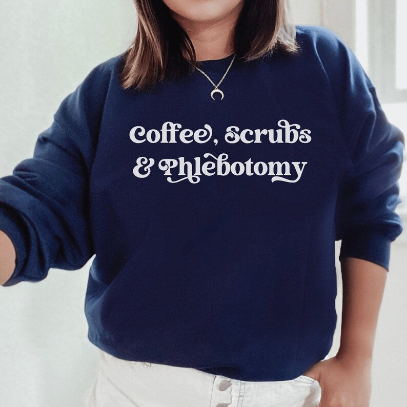 our gifts for a phlebotomist include this navy blue unisex sweatshirt that says coffee, scrubs, & phlebotomy