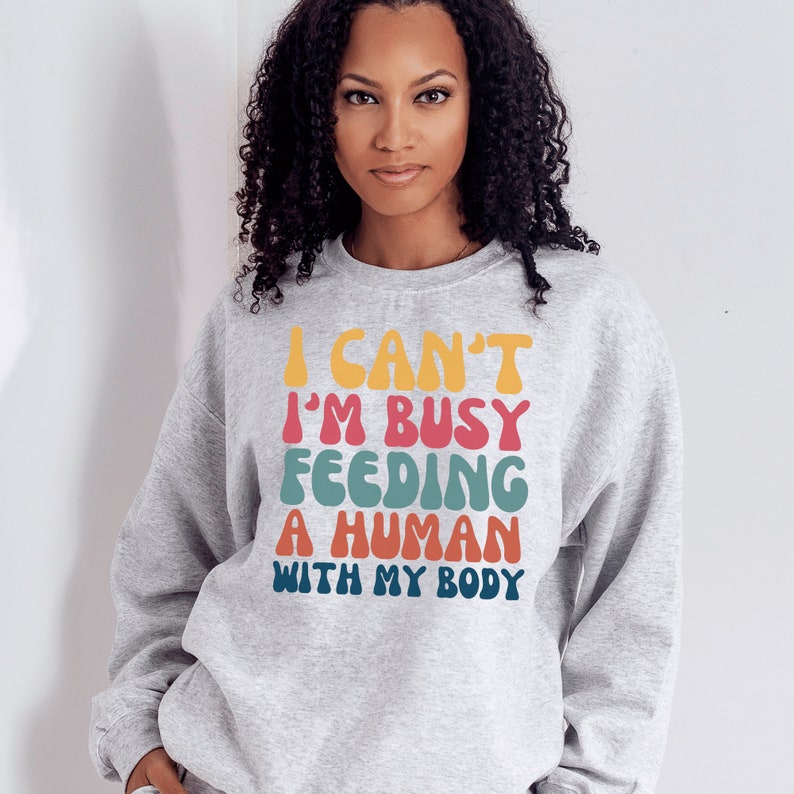 light gray unisex breastfeeding sweatshirt that says I can't i'm busy feeding a human with my body in retro capital letters makes the best Breastfeeding Mom Gifts