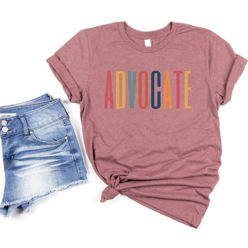 heather mauve unisex t-shirt that says the word "advocate" in capital, multicolored letters