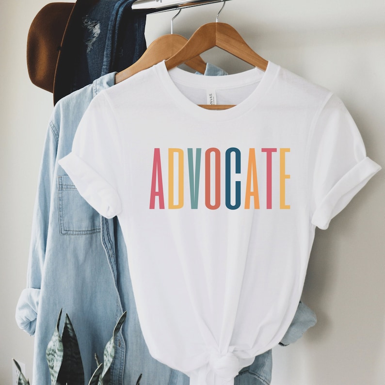 white unisex t-shirt that says the word "advocate" in capital, multicolored letters