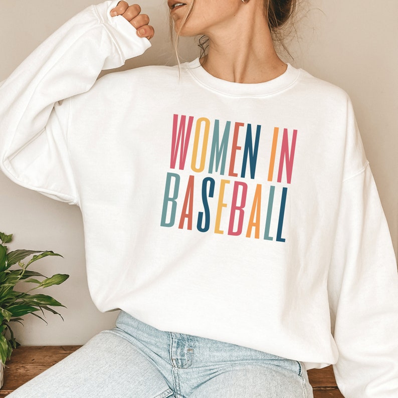 White unisex sweatshirt with multicolored letters that say women in baseball in all caps