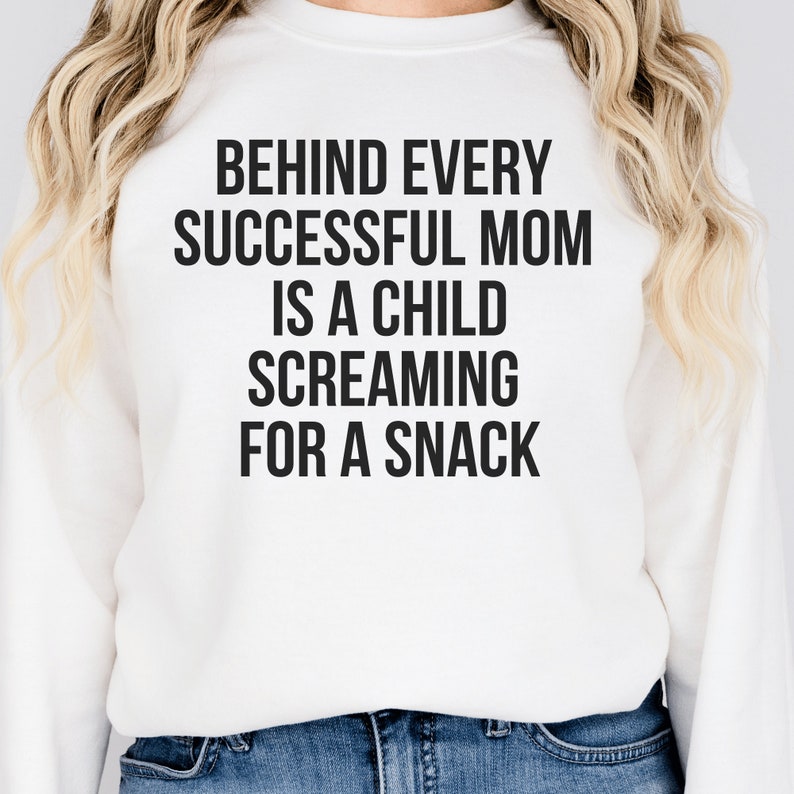 white unisex funny mom sweatshirt on female model that says behind every successful mom is a child screaming for a snack in black lettering. Perfect gift for a mompreneur or working mom.