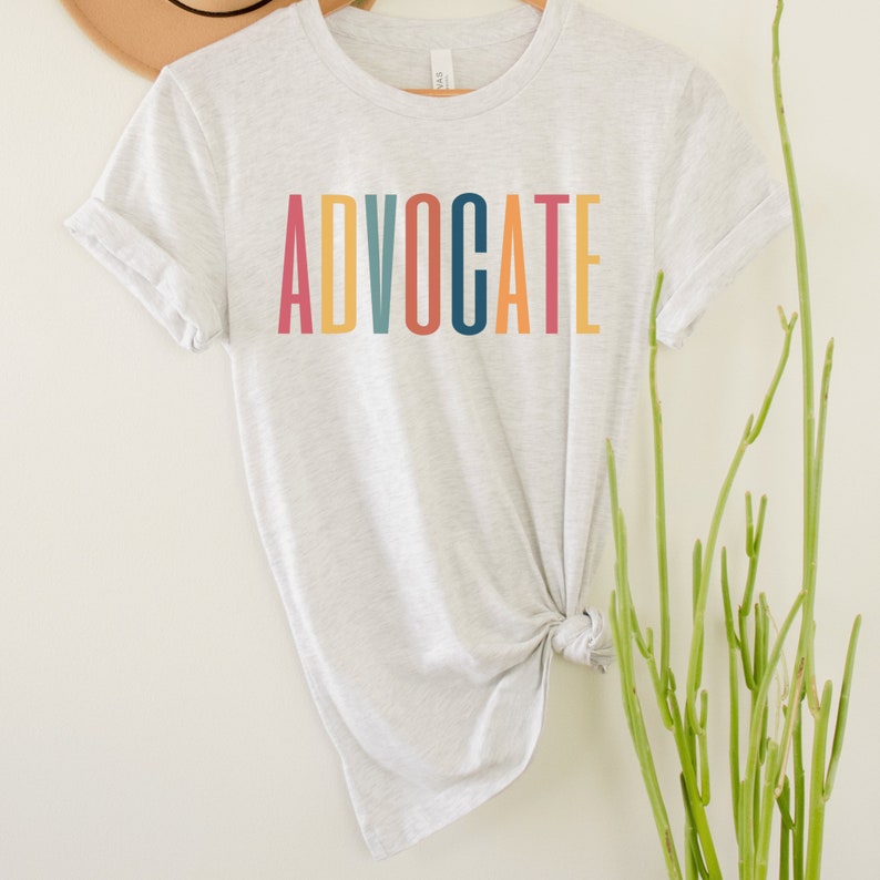 light gray unisex t-shirt that says the word "advocate" in capital, multicolored letters