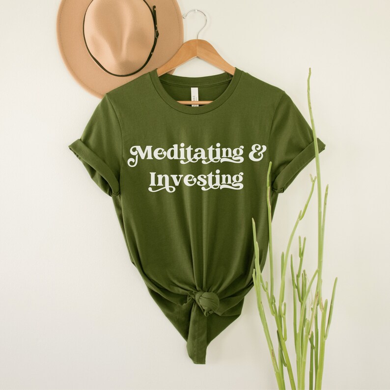 Olive unisex t-shirt on female model with a design that says "meditating and investing" in white lettering with a unique font. Perfect gift for someone interested in personal finance, meditation, and investing. 