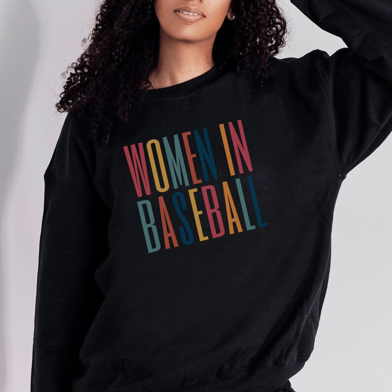 Black unisex sweatshirt with multicolored letters that say women in baseball in all caps