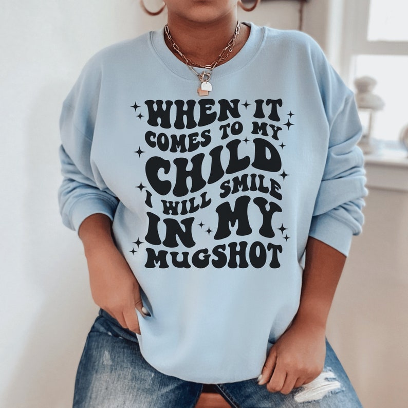 light blue unisex "mama sweatshirt" that says when it comes to my child i will smile in my mugshot in all capital retro styled black letters