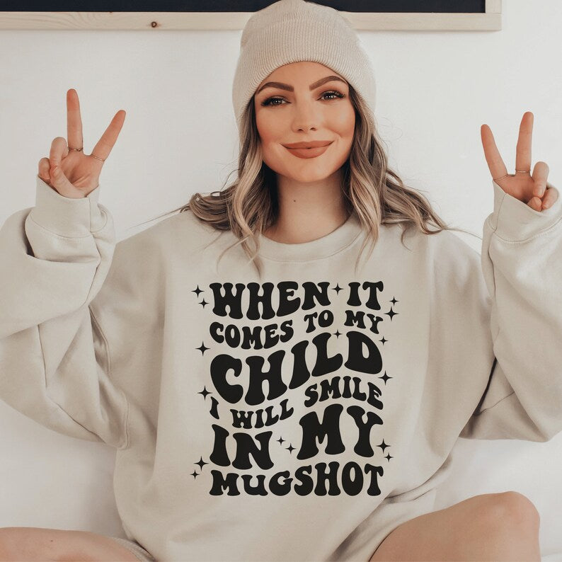 beige unisex "mama sweatshirt" that says when it comes to my child i will smile in my mugshot in all capital retro styled black letters