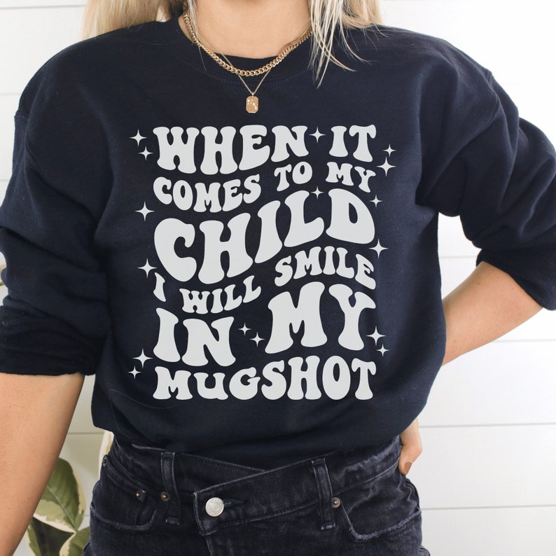 black unisex "mama sweatshirt" that says when it comes to my child i will smile in my mugshot in all capital retro styled white letters