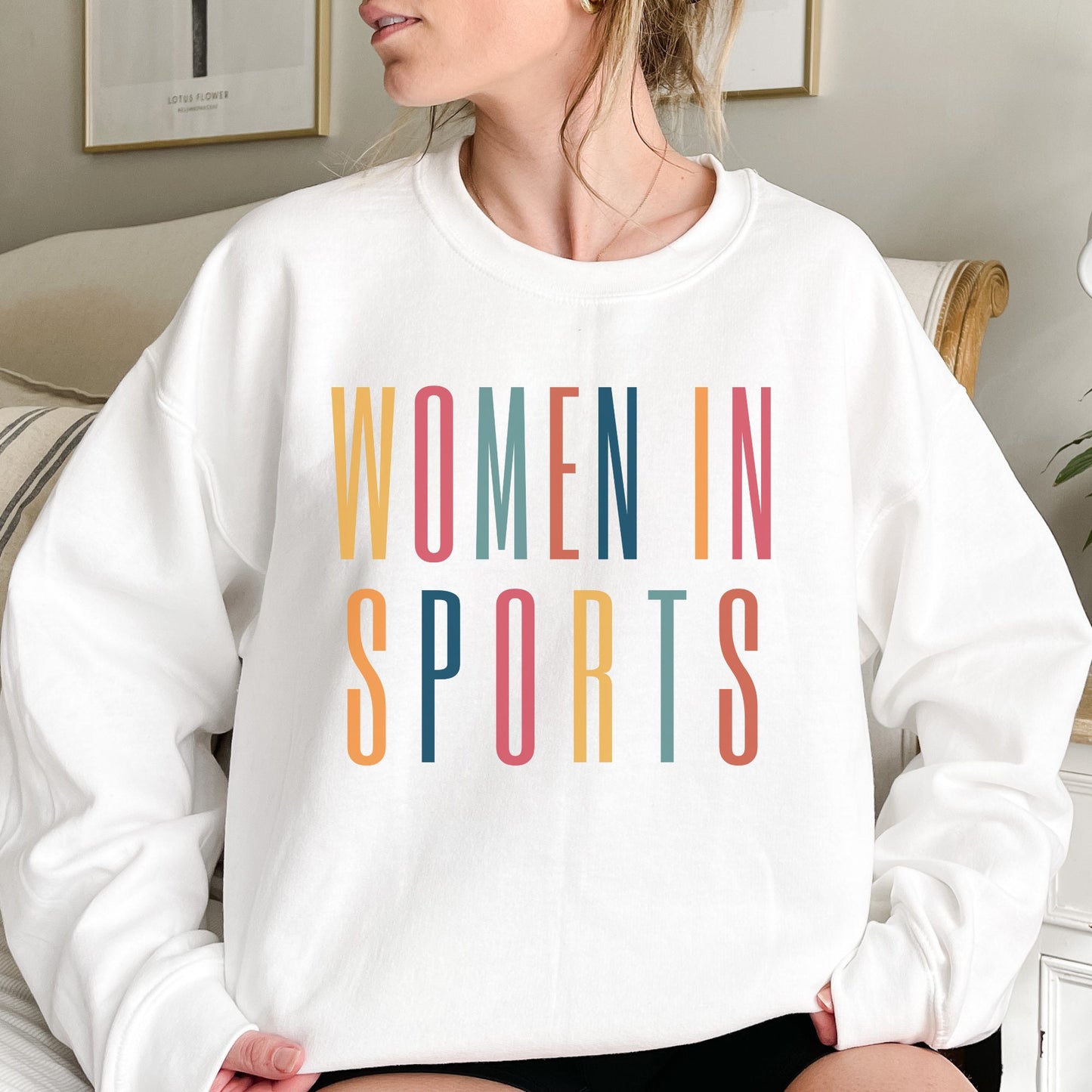 white unisex sweatshirt that says women in sports in capital, multicolored letters
