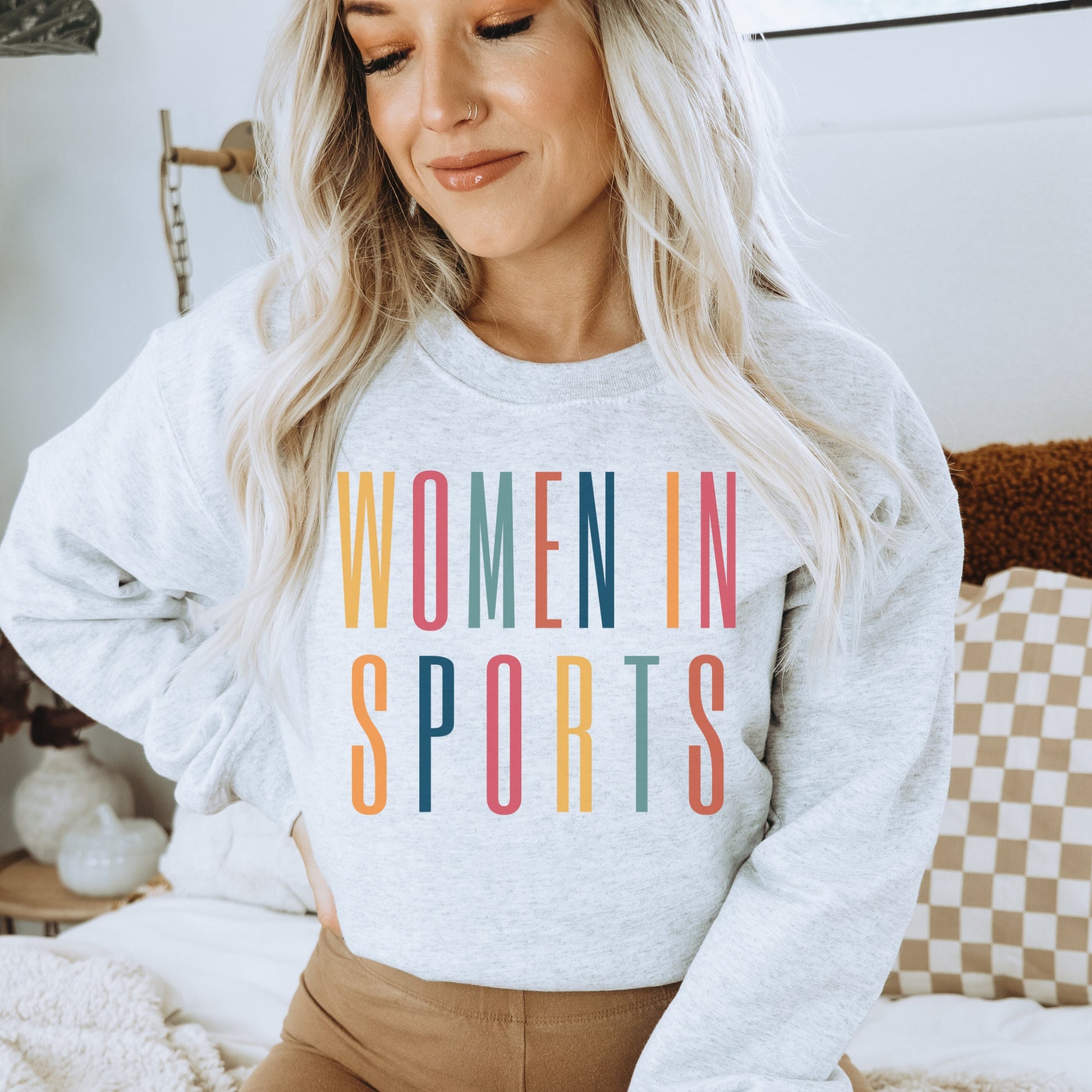 light gray unisex sweatshirt that says women in sports in capital, multicolored letters