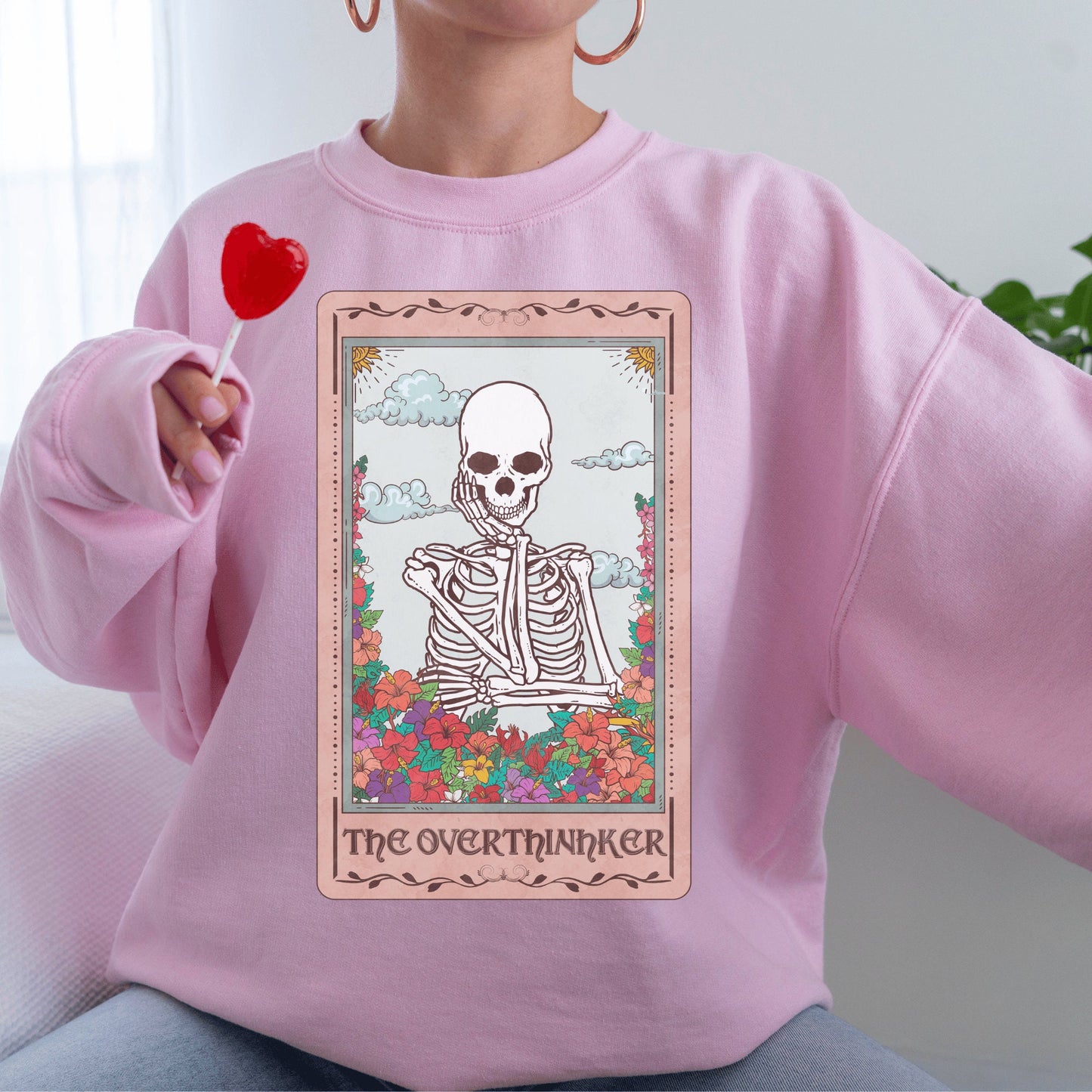 pink unisex overthinker sweatshirt with a graphic of a tarot card with skeleton graphic that says the overthinker
