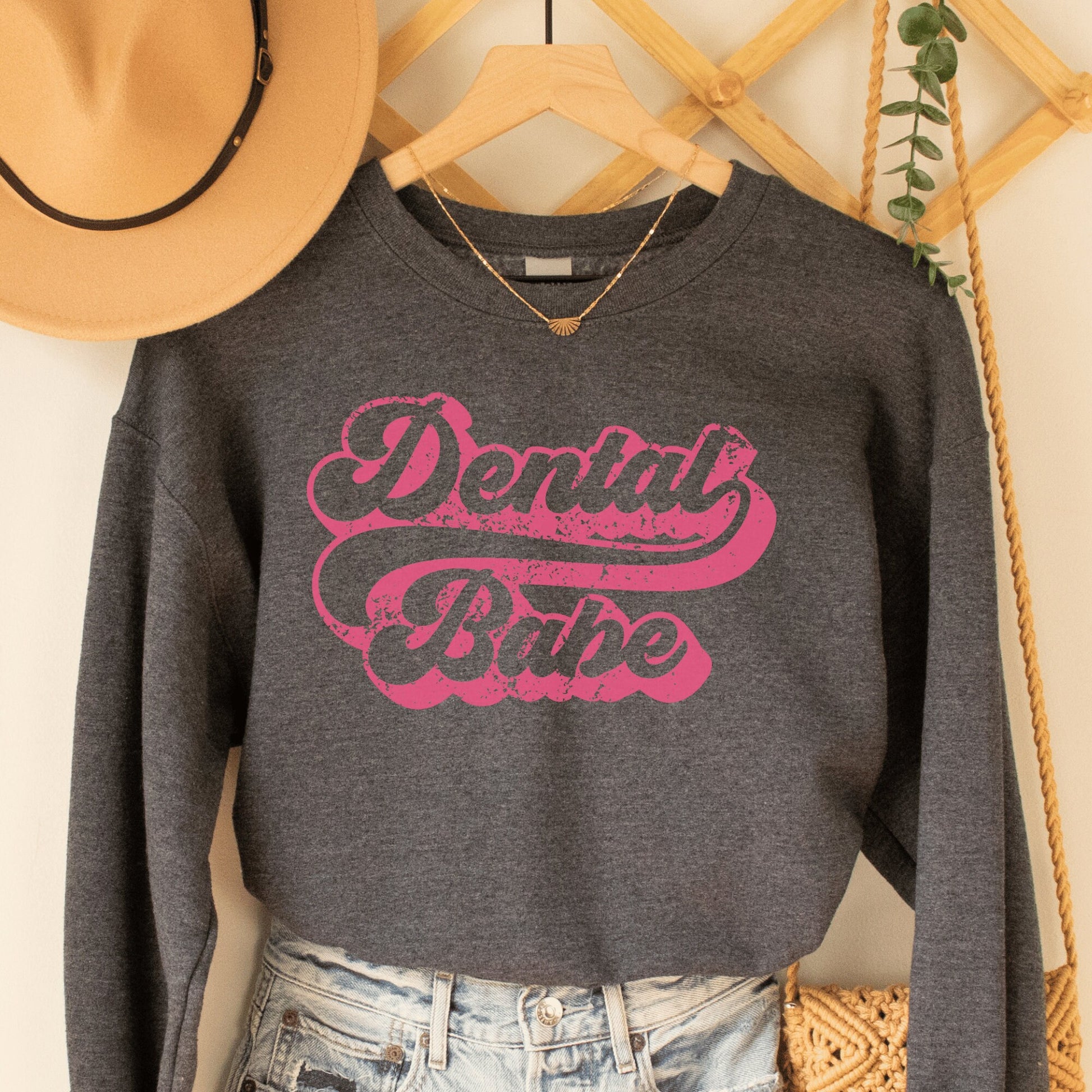 dark gray heather unisex dental hygienist sweatshirt that says "dental babe" in retro styled pink lettering with an antique and vintage style