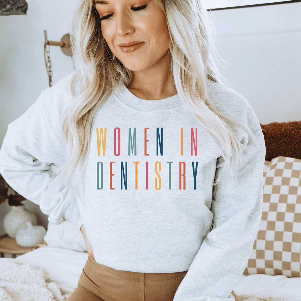 light gray unisex sweatshirt that says "women in dentistry" in all capital multicolored letters, perfect graduation gifts for dentists