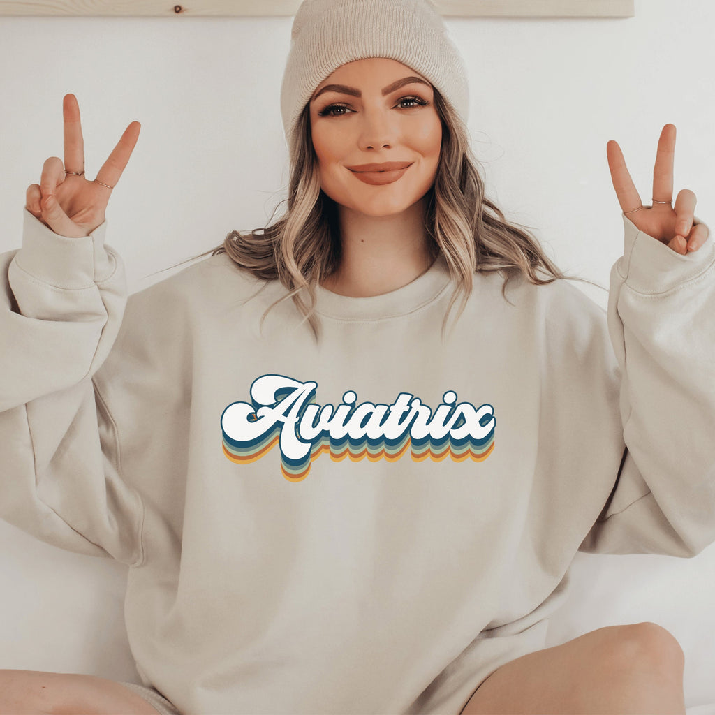 beige unisex sweatshirt with retro styled lettering with shadowing that says Aviatrix. female pilot shirts
