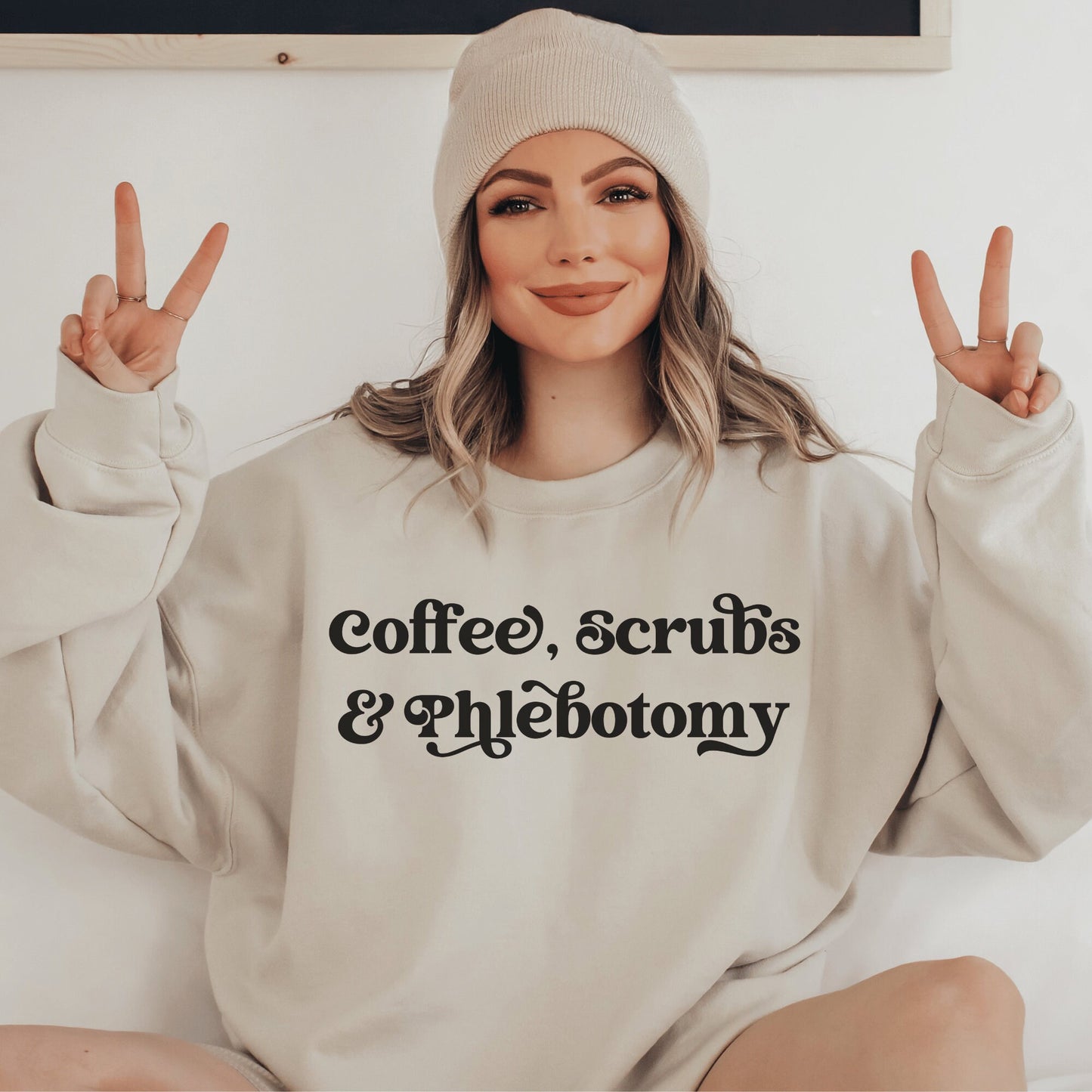 our gifts for a phlebotomist include this beige unisex sweatshirt that says coffee, scrubs, & phlebotomy