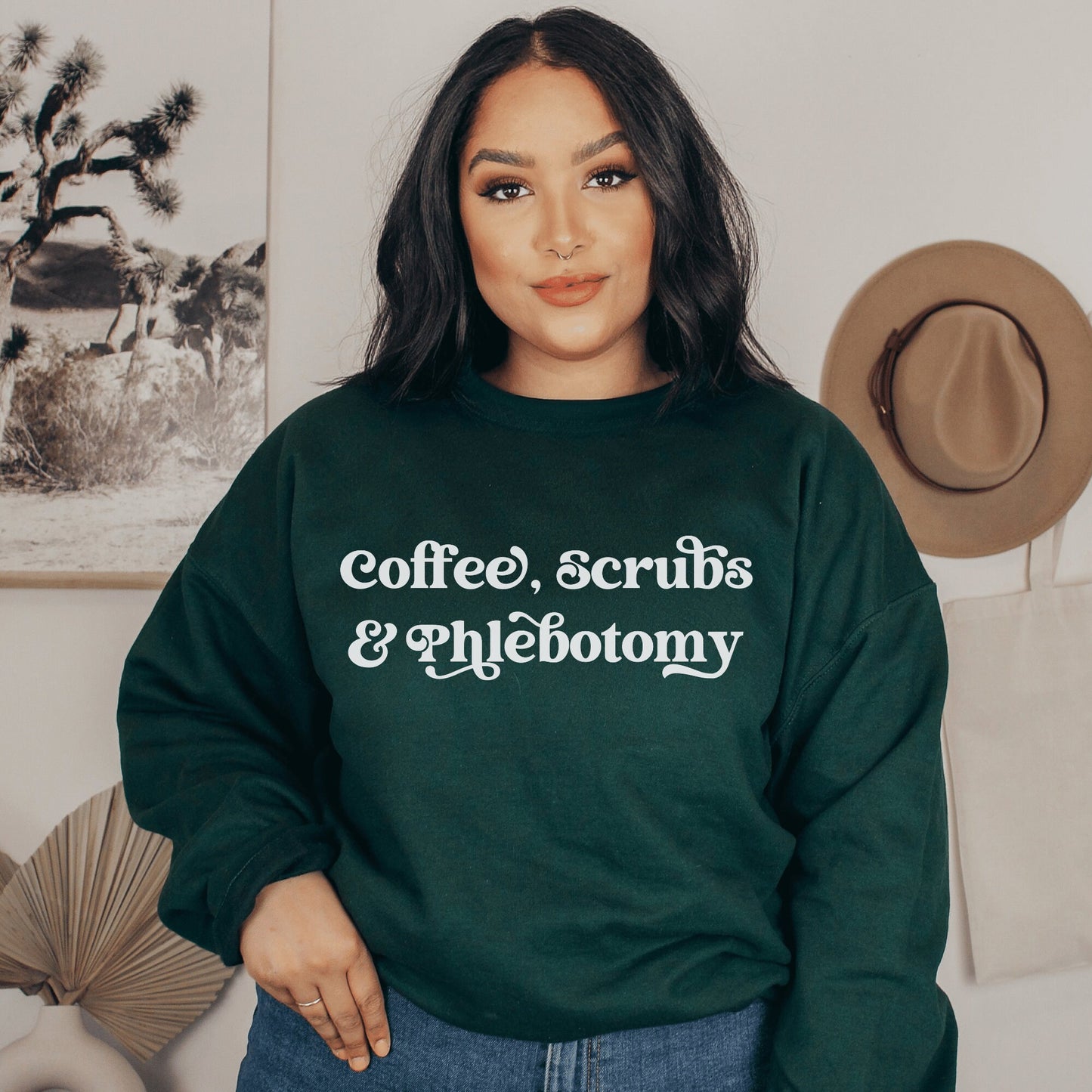 our gifts for a phlebotomist include this forest green unisex sweatshirt that says coffee, scrubs, & phlebotomy