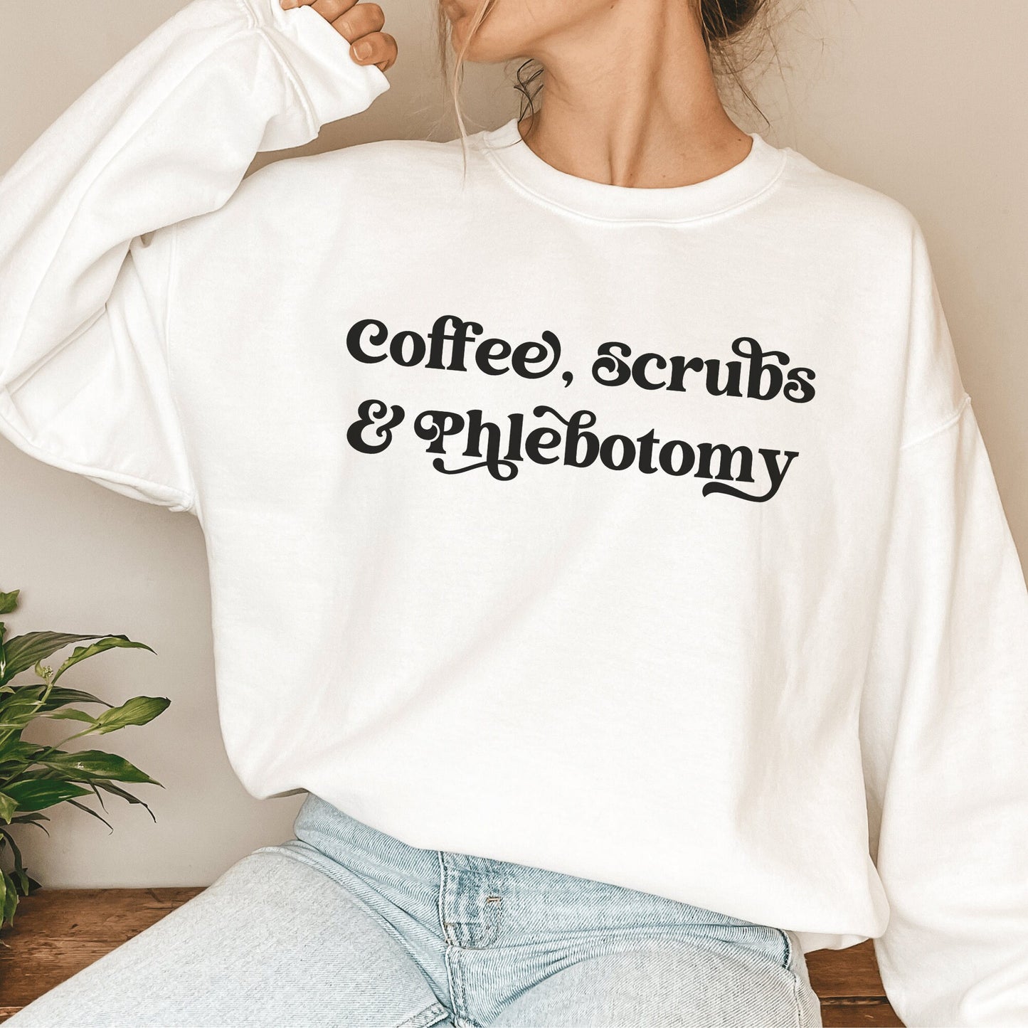 our gifts for a phlebotomist include this white unisex sweatshirt that says coffee, scrubs, & phlebotomy