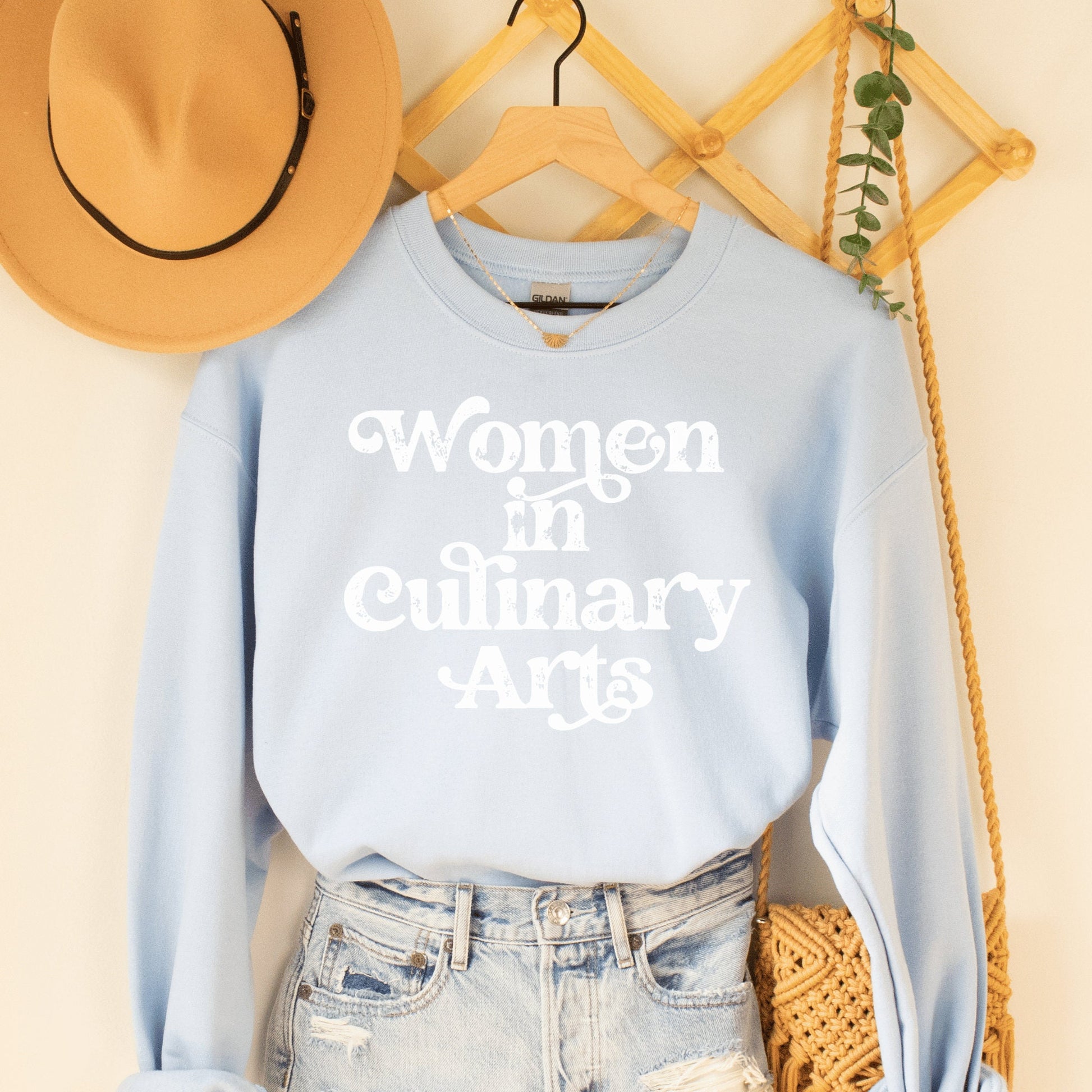 light blue unisex sweatshirt that says women in culinary arts in white letters with a whimsical font; perfect gift for culinary students