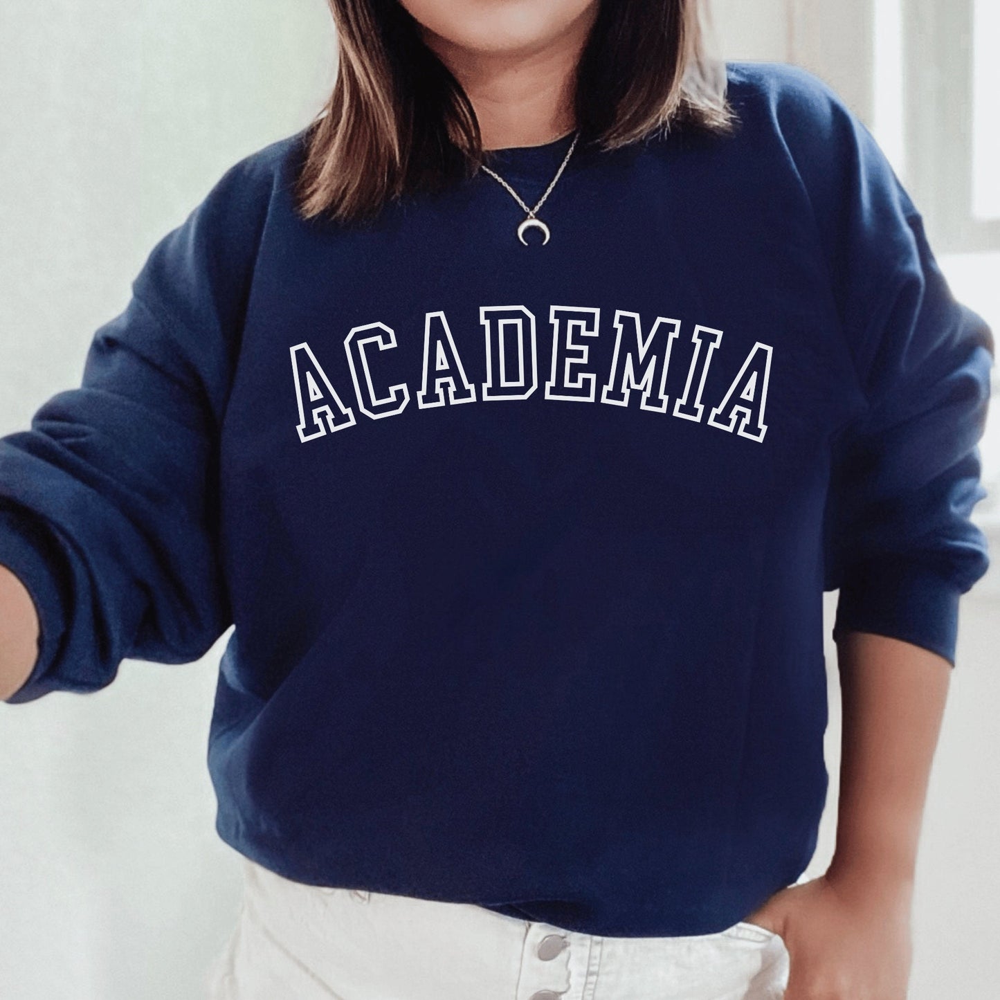 professor gifts, navy blue unisex sweatshirt on a female model that says Academia across the front in college style white letters