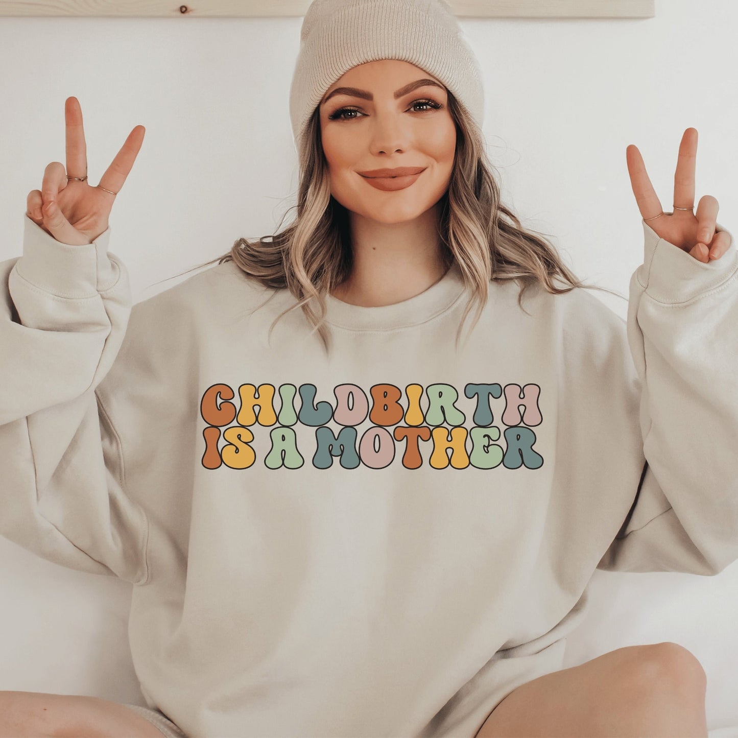 beige unisex motherhood sweatshirt that says "childbirth is a mother" in retro styled multicolored all capital letters