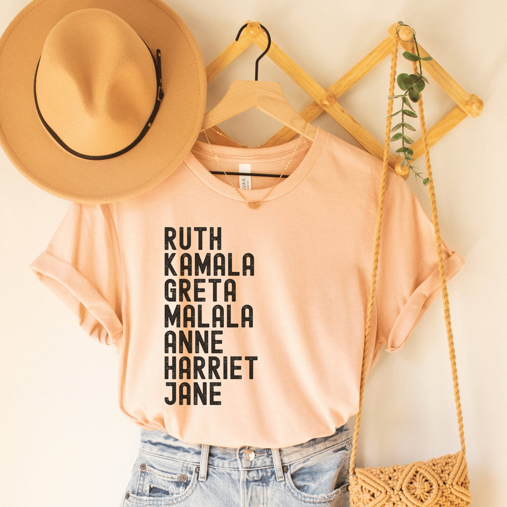 heather peach unisex empowered woman shirt that says ruth, kamala, greta, malala, anne, harriet, jane in all black capital letters