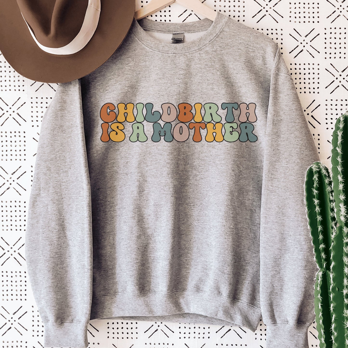 gray unisex motherhood sweatshirt that says "childbirth is a mother" in retro styled multicolored all capital letters