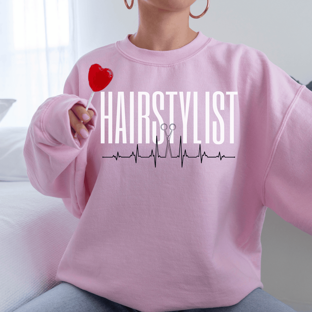 pink  unisex hairstylist sweatshirt that says the word hairstylist in all white capital letters with a heartbeat ekg design with scissors in the middle of the heartbeat
