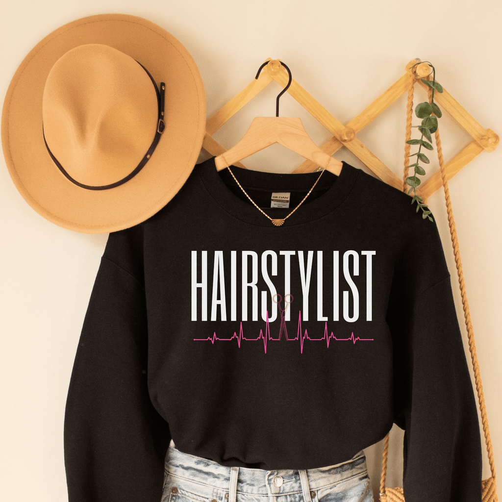 black  unisex hairstylist sweatshirt that says the word hairstylist in all white capital letters with a heartbeat ekg design with scissors in the middle of the heartbeat
